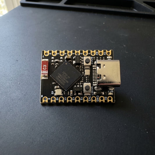 ESP32-S3 Supermini Development Kit placed on a workbench, showing the compact development board with USB Type-C connector, ESP32-S3 chip, onboard buttons, and gold-plated pin headers in a real-world workspace.